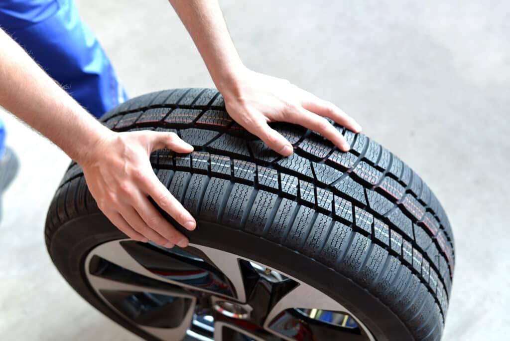 Mains d'un mécanicien inspectant la bande de roulement d'un pneu de voiture neuf dans un garage. Préparation à l'entretien ou au changement.