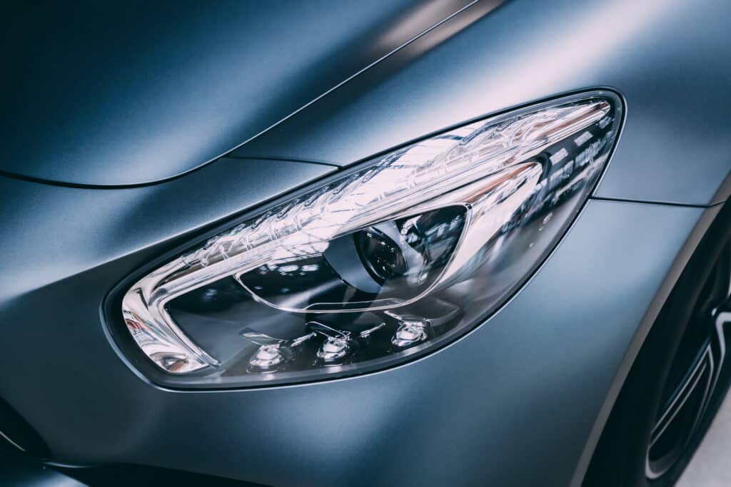 Gros plan sur le phare avant élégant d'une voiture sport gris-bleu mat, avec des détails LED et des reflets lumineux.