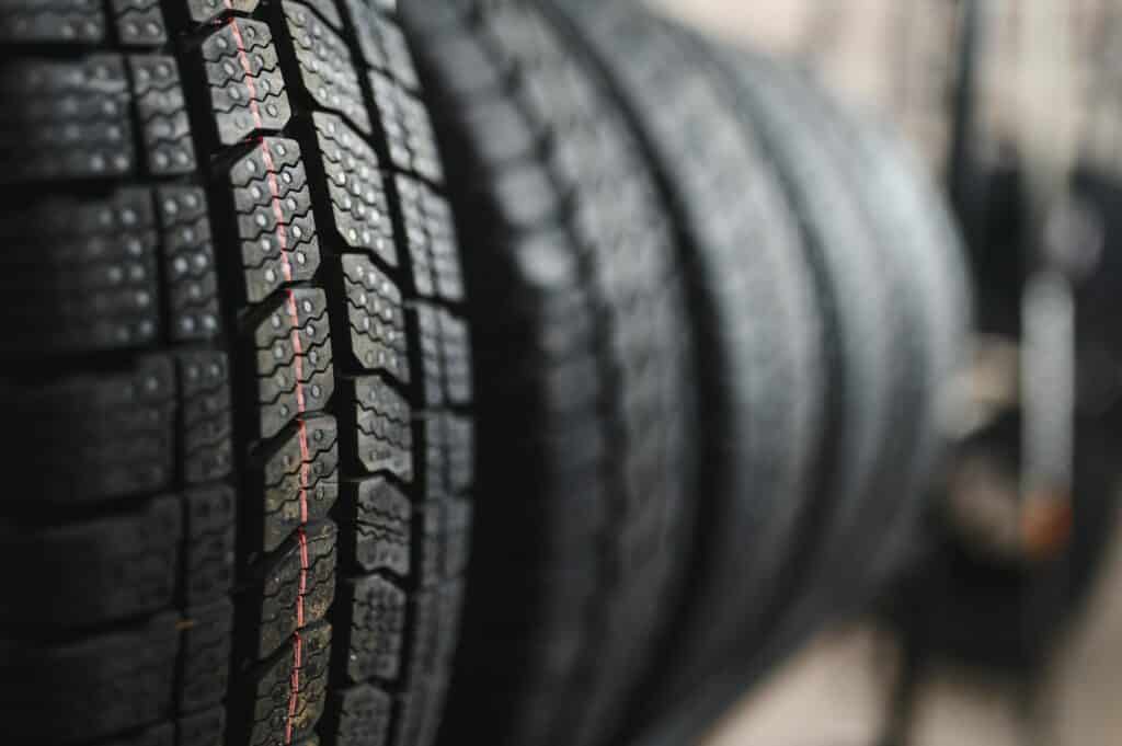 Gros plan sur des pneus d'hiver neufs empilés, montrant une bande de roulement détaillée avec une ligne rouge sur le côté.
