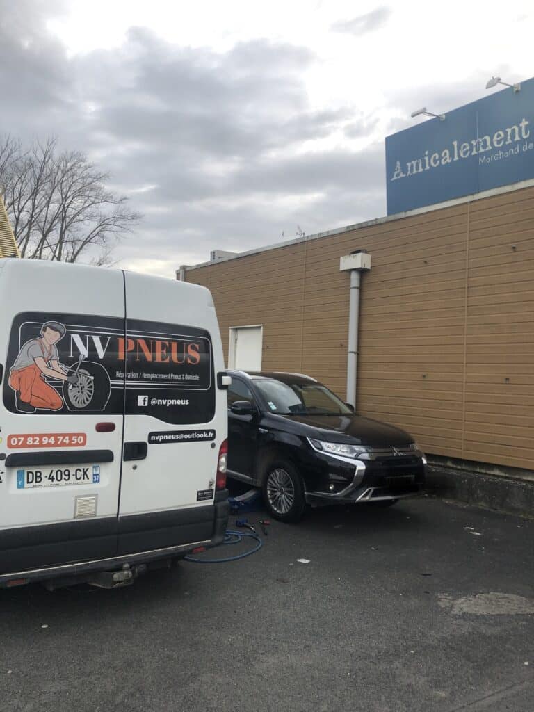 Fourgon NV Pneus blanc offrant réparation et remplacement de pneus à domicile pour un SUV noir levé sur un cric.