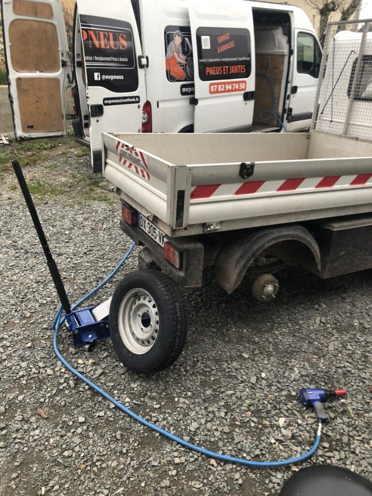 Service de pneus à domicile par NVPNEUS: une camionnette équipée sur gravier, un cric et une clé à chocs pour changer une roue d'un utilitaire. Tel: 07 82 94 74 50.